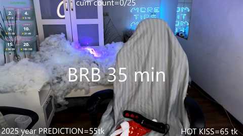 Media: Video of a man wearing a gray hooded robe, seated in a room with a whiteboard displaying \"BRB 35 min\" and \"cum count: 25+.\" Background includes a pile of white towels, a wooden floor, and a blue neon sign.