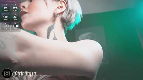 Media: Video of a pale-skinned woman with short, platinum-blonde hair, wearing a black top. She has a black feather tattoo on her neck and is seen from a low angle.