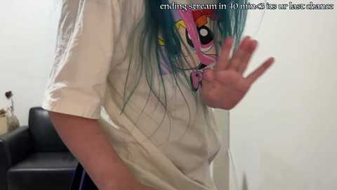 Media: A video of a woman with teal hair, wearing a white T-shirt, making a peace sign, standing in front of a black couch. Text overlay reads: \"enjoy screaming in 40+ places for 40+ minutes.\