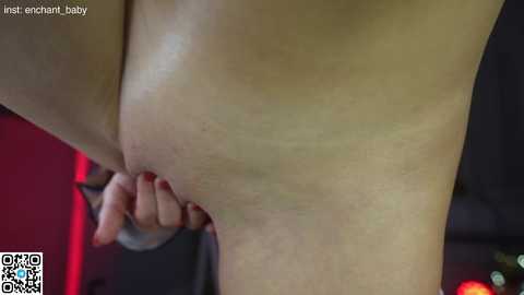 Media: A close-up video of a woman's bare buttocks, with one hand holding the skin taut, revealing the texture of her skin. The background is blurred, featuring a red and black gradient.