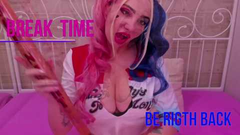Video of a pale-skinned woman with long, multicolored hair (pink and blue) wearing a revealing, wet, white and red Joker-themed top, holding a baseball bat, in a pink bedroom. Text reads \"BREAK TIME\" and \"BE RIGHT BACK.\