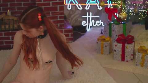 Media: Video of a nude, fair-skinned woman with long red hair, wearing a black collar, sitting on a white carpet. Background features a Christmas tree, wrapped presents, and a brick fireplace.