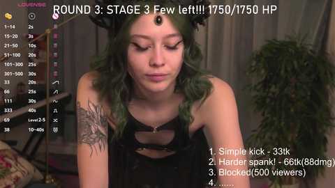 Media: A video of a young woman with green hair, wearing a black corset, and a black headpiece, in a dimly lit room with a green plant.