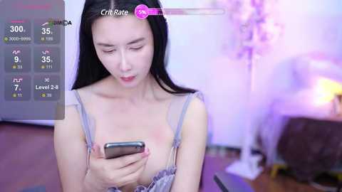 Media: A video shows an East Asian woman with long black hair, wearing a light blue bra, looking at her smartphone in a purple-lit room.