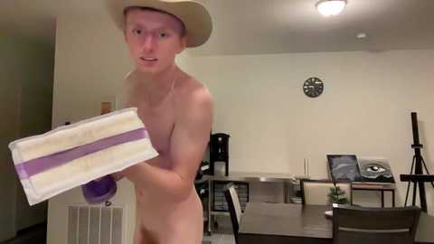 Media: Video of a naked, pale-skinned man with a cowboy hat, holding a slice of cake, in a dimly lit, beige room with a clock and a desk.