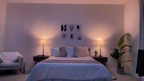 Media: Video of a minimalist, cozy bedroom with a white bed, two nightstands, a chair, and a potted plant. The walls are white, and there are abstract art prints on the headboard.