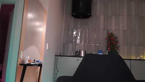 Media: A video of a modern kitchen with a dark countertop, a stainless steel stove, and a Christmas tree adorned with red ornaments and lights. The background features tiled walls and a black range hood.