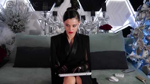 Media: Video of a woman with dark hair in a bun, wearing a black suit and gloves, typing on a keyboard in a chic, modern room with white hexagonal panels and Christmas decorations.