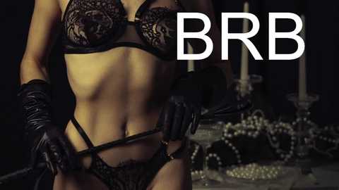 Media: Video of a fit, light-skinned woman in black lace lingerie and black gloves, holding a black strap, in a dimly lit, gothic-style room with candelabras and pearls. Text \"BBR\" overlays the image.