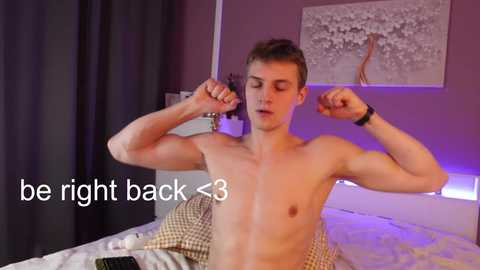 Media: Video of a shirtless, muscular, fair-skinned young man with short brown hair flexing his biceps in a bedroom with a white bed, purple lighting, and a black curtain. Text reads, \"be right back <3\".