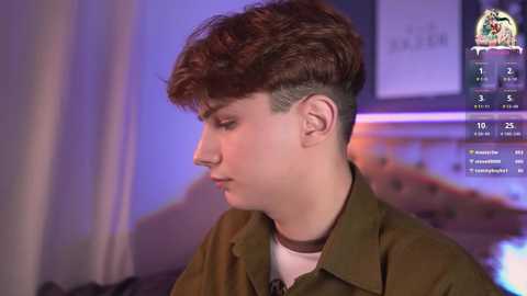 Media: Video of a young boy with short, dark hair and a buzz cut, wearing a green jacket over a white shirt. Background features a blurred, indoor setting with purple lighting and a social media interface displaying his profile.