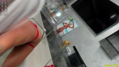 Media: Video of a woman in red lingerie and white stockings standing in a mirrored room with a black leather chair and colorful posters on the wall.