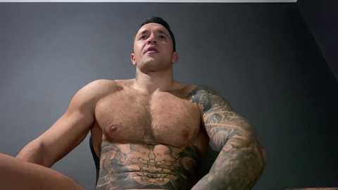 Media: Video of a muscular, tattooed man with short dark hair, wearing a black tank top, against a plain gray background.