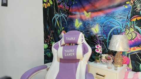 Media: A vibrant video of a purple and white gaming chair with \"Taurx Gamer\" logo, placed against a whimsical, colorful mural of a forest and a glowing mushroom, featuring a night sky.