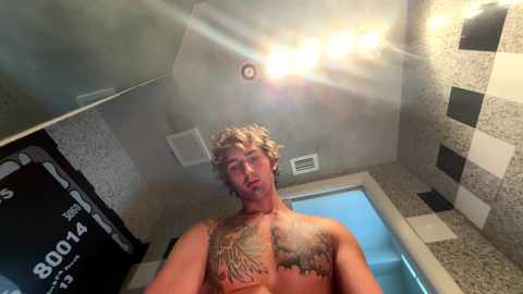 Media: Video of a shirtless, muscular man with curly blonde hair, tattoos on his chest and arms, standing in a steamy, tiled shower with a tiled wall and a black towel rack.