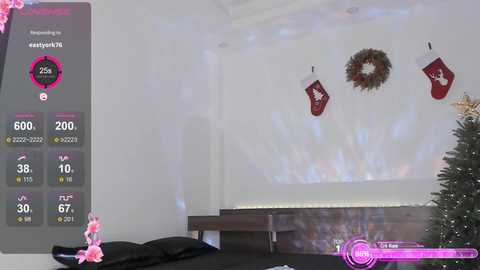 A video of a modern, minimalist bedroom with a cozy Christmas theme featuring a decorated tree, red stockings, and a wreath on a white wall. A digital overlay shows fitness stats on a scale.