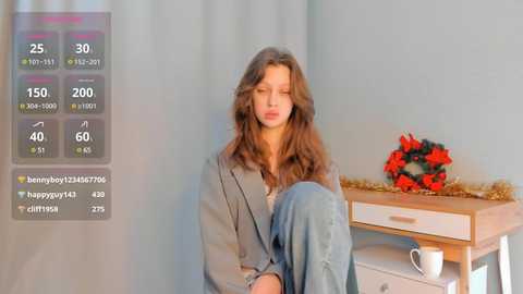 Media: A video of a young woman with wavy brown hair, wearing a gray cardigan and blue jeans, sitting on a wooden table. Behind her, a floral arrangement and a digital fitness app display on a smartphone.