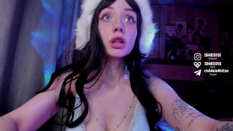 Media: Video of a young woman with fair skin, long black hair, wearing a white furry headband, a revealing lace bralette, and a tattoo sleeve. Background shows a dimly lit room with posters.