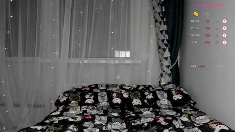 Video of a bedroom with a black bedspread featuring Star Wars characters, a sheer white curtain, and a white wall with digital clock and weather display.