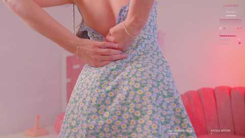 Media: Video of a woman in a floral dress, adjusting the dress strap, with a pink background and red lighting.