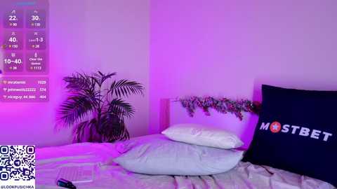 Media: Video of a minimalist bedroom with a white bed, dark pillow, and \"MOSTBET\" pillow, purple lighting, and a plant in the corner.