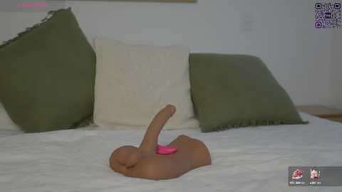 Media: Video of a brown-skinned, nude man lying on a white bed with green and white pillows, holding a pink vibrator between his legs.