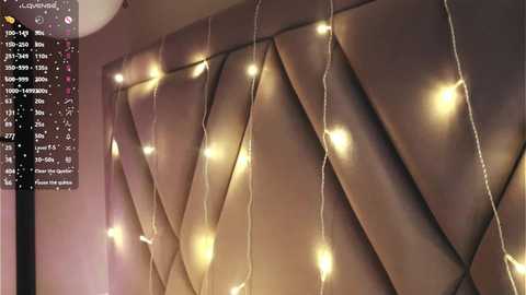 Media: Video of a cozy bedroom with a tufted headboard featuring warm, glowing fairy lights. The background includes a digital interface with various settings and options.