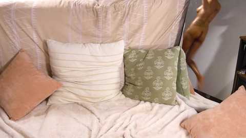 Media: Video of a plush white couch with beige and green patterned pillows, a mannequin standing in the background, and a beige blanket draped over the sofa.