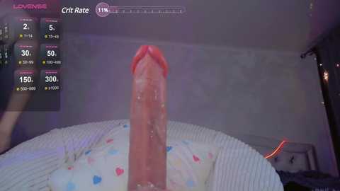 Media: A video of a man's erect penis, glistening with sweat, viewed from the front, set against a dimly lit bedroom with a white bedsheet and a blurred background.