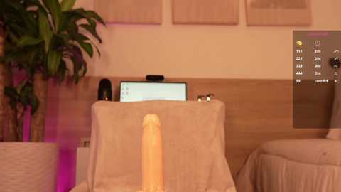 Video of a modern living room with beige furniture, a potted plant, a flat-screen TV, and a large dildo on a table, under ambient lighting.