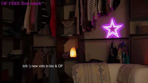 Media: Video of a dimly lit, cluttered closet with hanging clothes, a neon star, and a glowing candle on a shelf. Text reads: \"OF FIRST WEEK\" and \"brb (new vids in big & OF).\