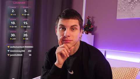 Media: A video of a young man with short dark hair, wearing a black shirt, sitting pensively in a room with purple walls and a Christmas tree.