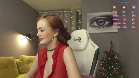 Video of a fair-skinned woman with red hair, wearing a red sleeveless top, seated in an Artix gaming chair in a modern living room.