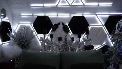 Media: A video of a futuristic, hexagonal-themed interior with white, glowing lights, featuring a minimalist arrangement of white and metallic ornaments on a green sofa.