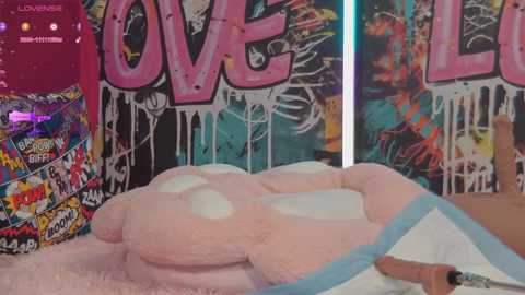 Media: Video of a pink, fluffy, plush teddy bear with white paint drips, covered in colorful graffiti. Background features a wall with \"LOVE\" and \"LOVE\" graffiti.