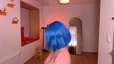 Media: Video of a person with bright blue bob haircut, standing nude in a minimalist room with white walls, wooden floor, and a mirror.