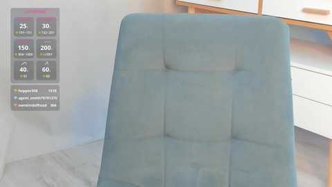 Media: Video of a modern, light blue upholstered chair with a tufted backrest in a minimalist room featuring a white dresser and a wooden table. A digital overlay on the left displays weather data in a gray box.