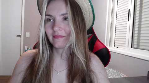 Media: A video of a smiling young woman with long blonde hair and a straw hat, sitting on a gaming chair with a green and red striped cushion.