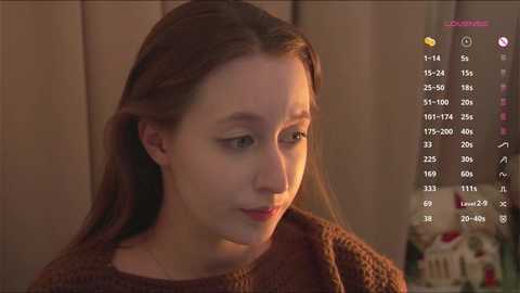 Video of a young woman with fair skin, brown hair, and brown sweater, gazing introspectively. Background shows wooden paneling and a gaming interface with text and icons.