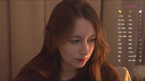 Video of a young woman with long brown hair, wearing a brown sweater, looking introspective in a dimly lit room. Overlay shows a game interface with options.