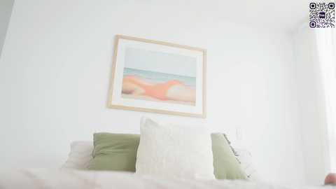 Media: A video of a minimalist bedroom with a white wall, a framed painting of a beach, and a bed with white and green pillows. The room is softly lit, creating a serene atmosphere.