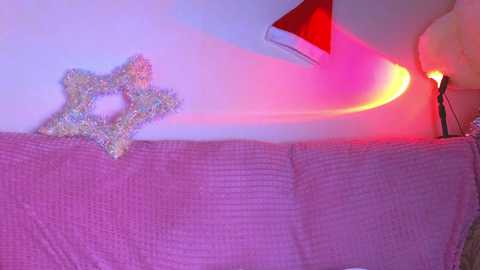 Media: Video of a cozy living room with a pink, textured couch and a decorative star-shaped, glittery ornament. A warm, pinkish light casts a soft glow on the scene, adding a festive, whimsical atmosphere.