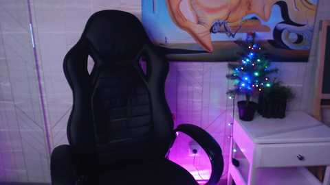 Media: Video of a black gaming chair with a textured backrest, positioned in front of a white desk with a blue fairy lights decoration and a framed anime artwork.