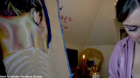 Media: A video of a woman painting a mural of a nude woman on a white wall, with a candlelit room in the background.