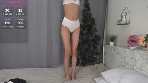 Media: Video of a slender, light-skinned woman wearing white lingerie, standing in a cozy bedroom with a grey curtain backdrop, digital health stats displayed, and a Christmas tree.