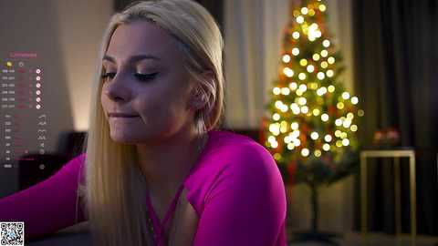 Media: A video of a blonde Caucasian woman with fair skin, wearing a bright pink top, looking serene. Background features a cozy living room with a Christmas tree and warm lighting.