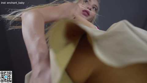 Media: Video of a blonde woman in a beige dress, seen from a low angle, emphasizing her large breasts and curvy figure.