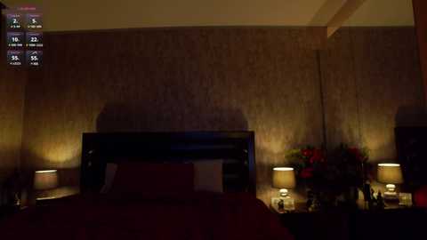 Media: Video of a dimly lit bedroom with a dark wooden bed, red bedding, and floral-patterned wallpaper. Nightstand lamps provide soft light. The room features a large window with blinds partially drawn.