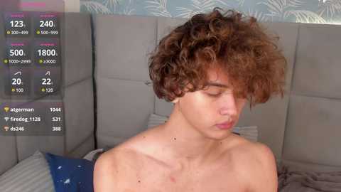 Media: Video of a shirtless young man with curly brown hair, sitting on a gray couch, with a digital health tracker overlay showing temperature, heart rate, and other metrics.