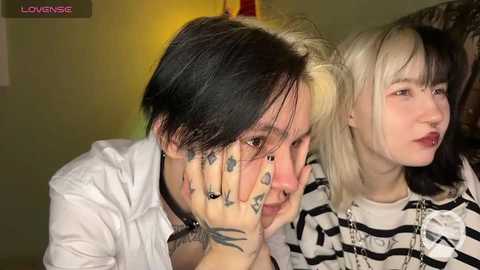 Media: Video of two young women with dark hair, one with a black choker, the other with a striped shirt, both with tattoos, in a dimly lit room.